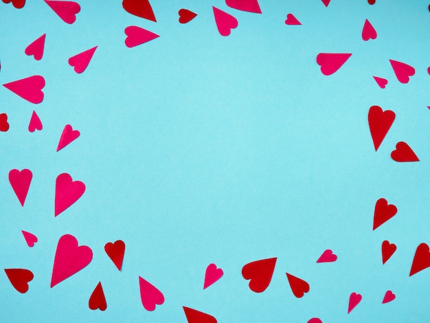 Top view of red and pink paper hearts in corner on blue surface with copy space