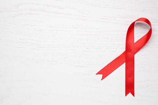 Photo top view of red ribbon on white wooden background space for text aids disease awareness