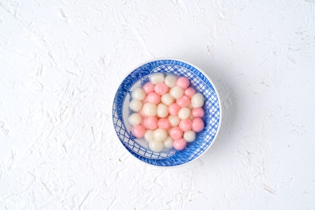 Top view of red and white tangyuan (tang yuan, glutinous rice dumpling balls) in blue bowl on white background for winter solstice festival food.