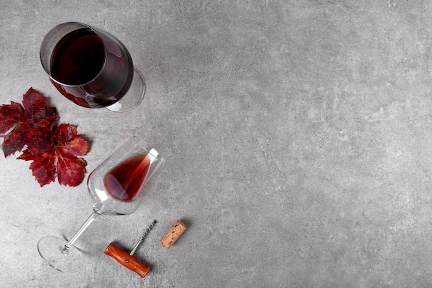 Vista dall'alto di bicchieri da vino rosso con foglie di uva autunnale rossa e cavatappi e tappo per vino su grigio