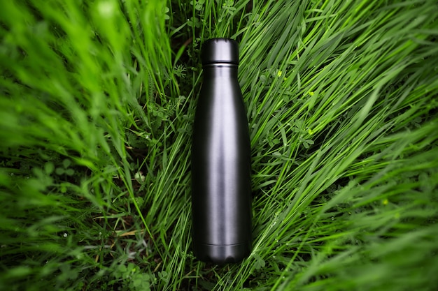 Top view of reusable, steel black bottle thermos for water in green grass. Zero waste. Environment concept. No plastic.