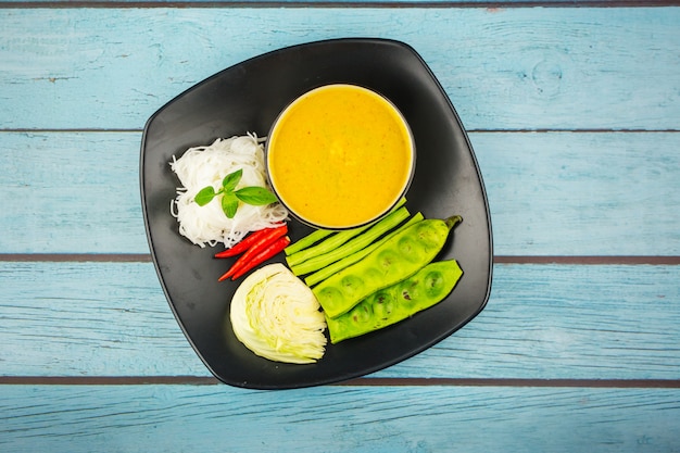 Top view Rice noodles in fish curry sauce with vegetables on a blue wood background