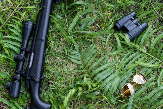 Top view rifle binoculars and sunglasses on grass floor