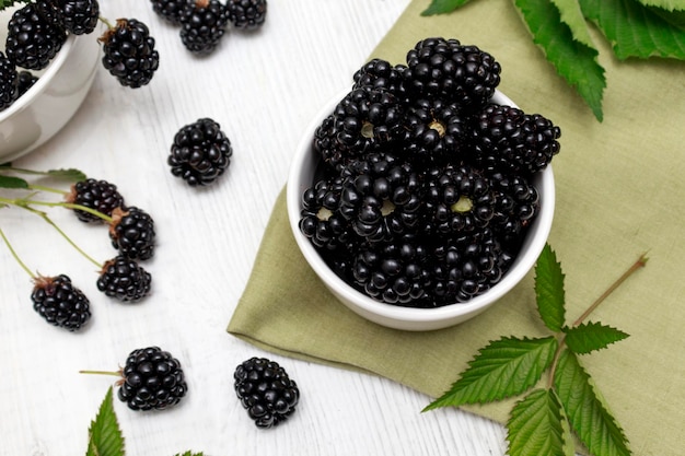 Top view of ripe blackberries with leaves in a plate on a wooden table Fruit berry background