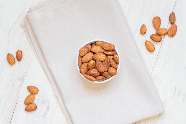 Top view of Roasted Almonds in white porcelain bowl on textile napkin