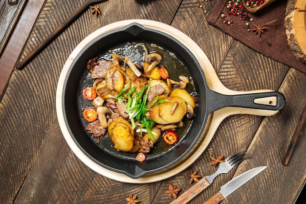 Top view on roasted potatoes and beef meat in cast iron pan