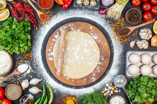 Top view of rolling pin over the circle dough on wooden cutting board and set of foods