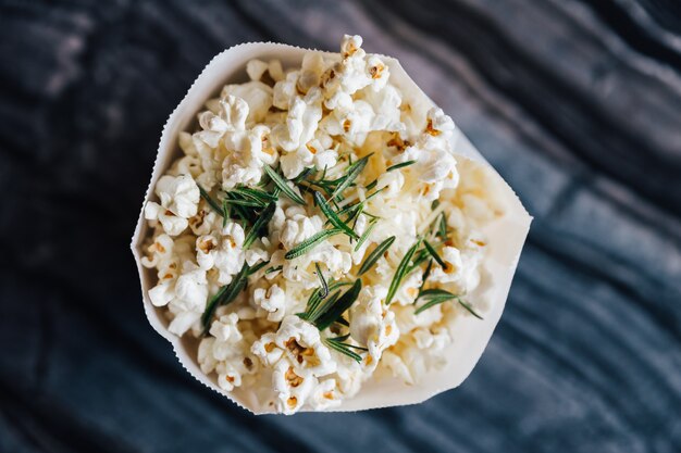 Top view of rosemary popcorn in paper bag on top marble table.