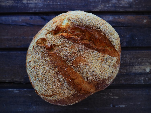 Вид сверху на круглый хлеб, вкусный свежий кукурузный хлеб с посыпкой на старом деревянном столе