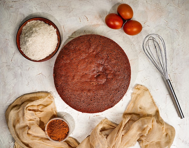 Vista dall'alto sul pan di spagna rotondo al cioccolato o sulla torta chiffona su carta da forno così morbida e deliziosa con ingredienti uova farina latte su tavola di legno concetto di panetteria fatto in casa per sfondo e carta da parati