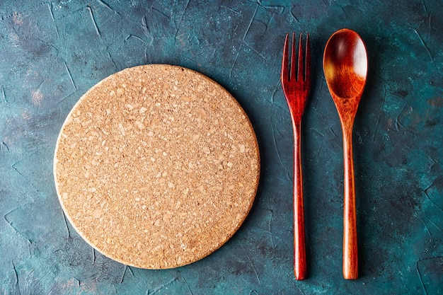 Top view of round cutting board between fork and spoon on rustic table background for menu with copy...