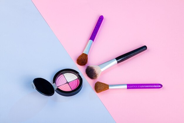 Top view of round eyeshadow palette with brushes blue and pink background