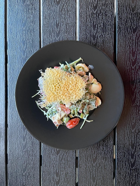 Top view of a salad with small eggs tomatoes sauce and\
decorated with baked parmesan crisp on a black plate nourishment\
browned chips potatoes cooked vegan breakfast organic food\
lunch