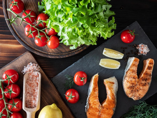 Top view of salmon arrangement with salad and tomatoes on wooden and stone trays