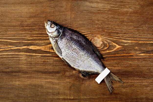 Top view of salted jerked roach fish with label on tail on rustic wooden background with copyspace