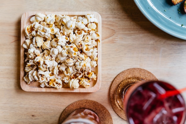 La vista superiore di popcorn salato è servito in piatto di legno quadrato sulla tavola di legno.