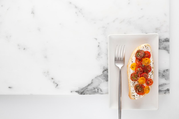 Foto vista dall'alto panino con crema di formaggio e pomodori sul piatto con forchetta e copia-spazio