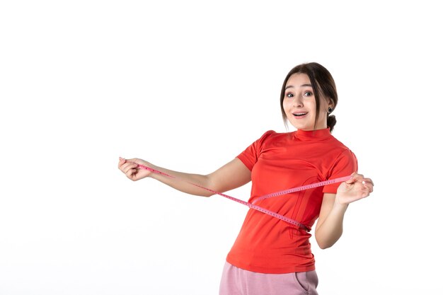 Top view of a satisfied young lady gathering her hair dressed in redorange blouse and holding metre measuring her waist on white background