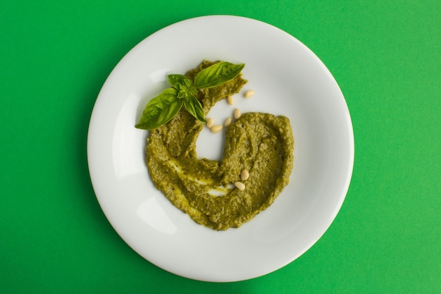 Top view of sauce pesto on the white plate on the green surface