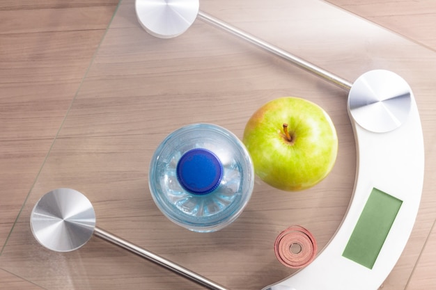 Top view of scale on wooden table with bottle of water, tape measure and an apple