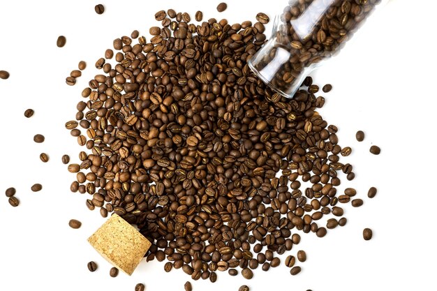 Top view of scattered coffee beans from glass bottle and cork isolated on white