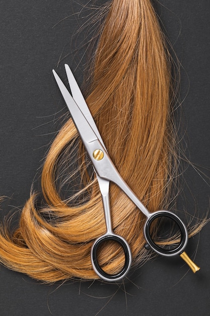 Top view of scissors and a cut off strand of children's blond hair on a dark paper background