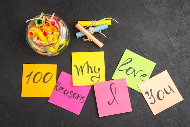 Photo top view scroll colored wish papers in jar reasons why i love you written on sticky notes on dark background