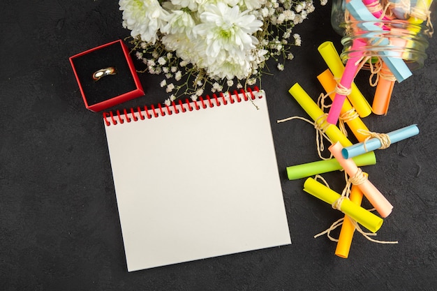 Top view scroll wish papers scattered from jar notebook ring in\
box flowers on dark background