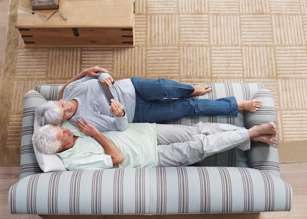 Top view senior couple and sofa with tablet social media online news app and ebook in lounge Happy old man woman and relax with digital technology subscription or website on internet connection