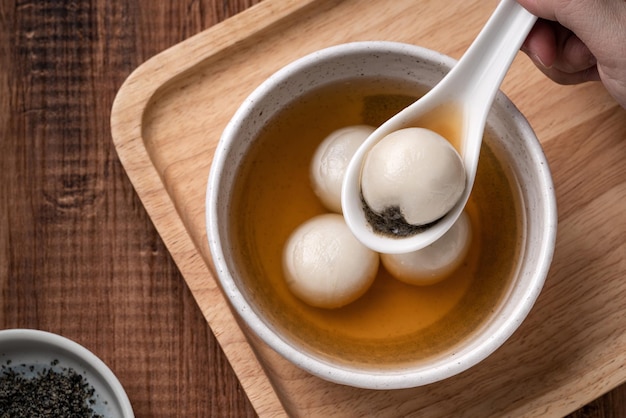 동지 축제 음식을 위해 나무 테이블 배경에 있는 그릇에 달콤한 시럽 수프를 넣은 참깨 큰 탕위안(탕 위안, 찹쌀 만두 공)의 꼭대기 전망.