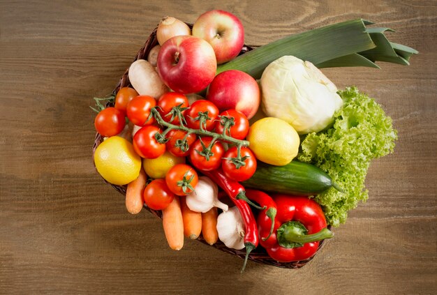 Top view of a set of vegetables and fruits in a wicker basket on a wooden background