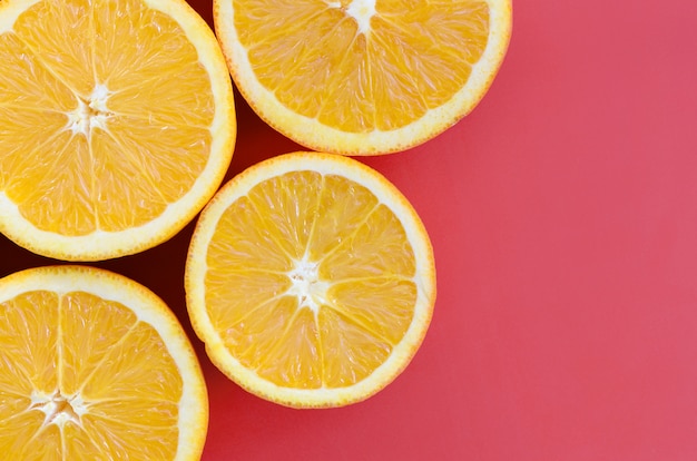 Top view of a several orange fruit slices on bright background in red color. A saturated citrus texture image