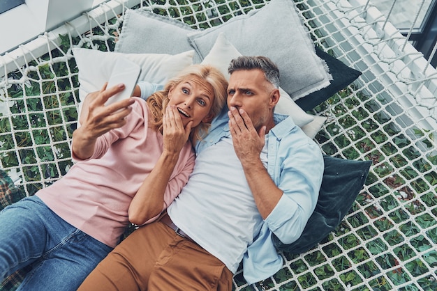 Top view of shocked mature couple looking at smart phone