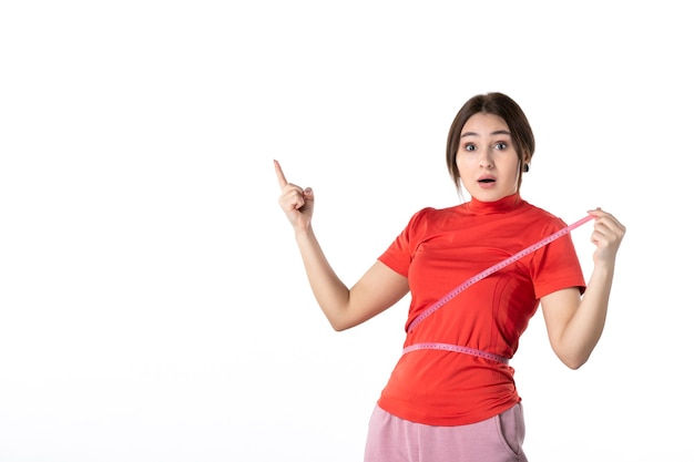 Top view of a shocked young lady gathering her hair dressed in redorange blouse and holding metre measuring her waist pointing up on white background