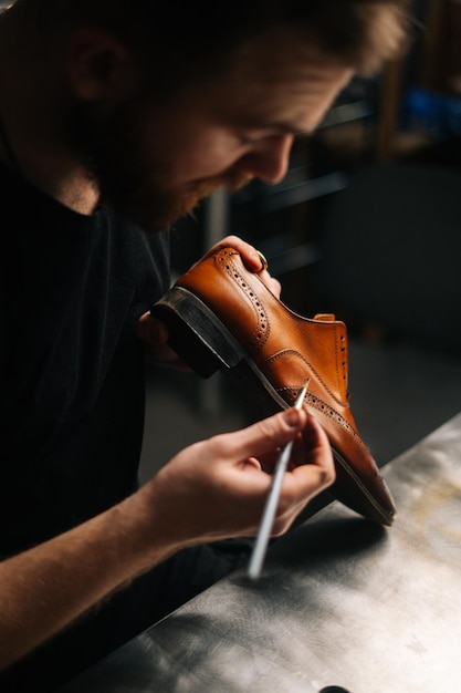 Top view of shoemaker painting heel and sole of light brown leather shoes with brush during restoration working. Concept of cobbler artisan repairing and restoration work in shoe repair shop.