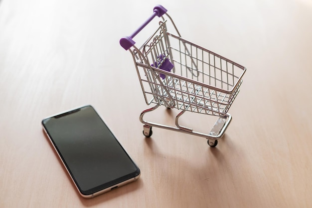 Foto vista dall'alto su un carrello della spesa e un telefono cellulare su un tavolo di legno shopping online per smartphone shopping online