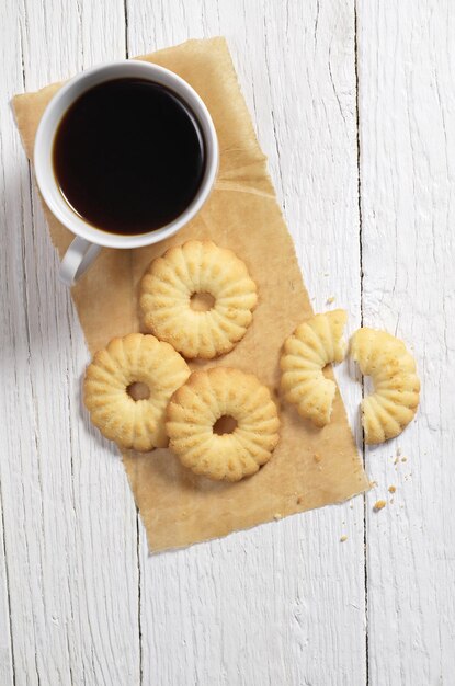 Top view of shortbread cookies and cup of coffee on white wooden table