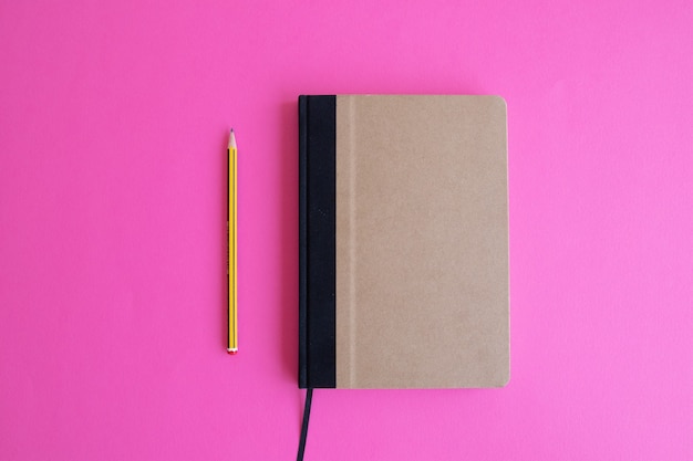 Top view shot of a beige planner and a yellow penc on a pink background