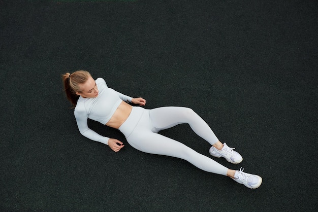 Top view shot of happy woman sitting on road after a morning run Fit woman on road taking a break after outdoor workout