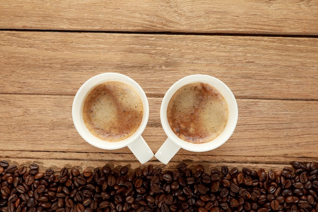 Фото Вид сверху выстрел из двух горячих свежий кофе в белой чашке с пеной и кофейных зерен