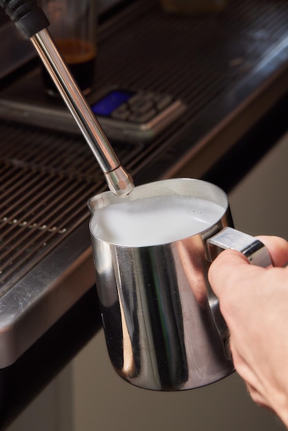 Снимок сверху профессионального бариста, наливающего молоко из банки в чашку кофе, готовящегося к употреблению