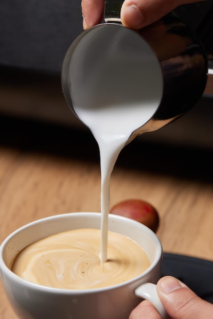 Top view shot of professional barista pouring milk from jar in to a cup of coffee coffee being prepa