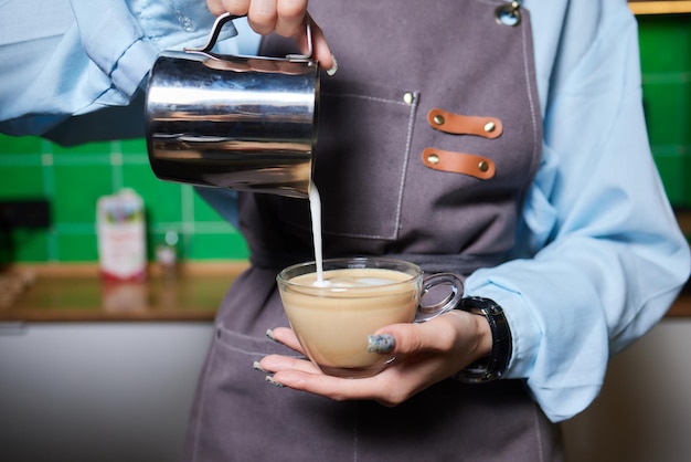 Colpo di vista dall'alto di un barista professionista che versa il latte dal barattolo in una tazza di caffè in preparazione