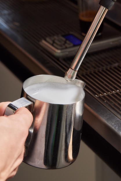 Top view shot of professional barista pouring milk from jar in to a cup of coffee coffee being prepared by a barista Focus on hands holding cup of coffee