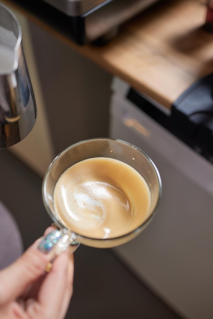 Top view shot of professional barista pouring milk from jar in to a cup of coffee coffee being prepared by a barista Focus on hands holding cup of coffee