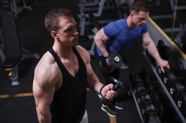 Top view shot of twin brothers bodybuilders exercising with dumbbells at gym