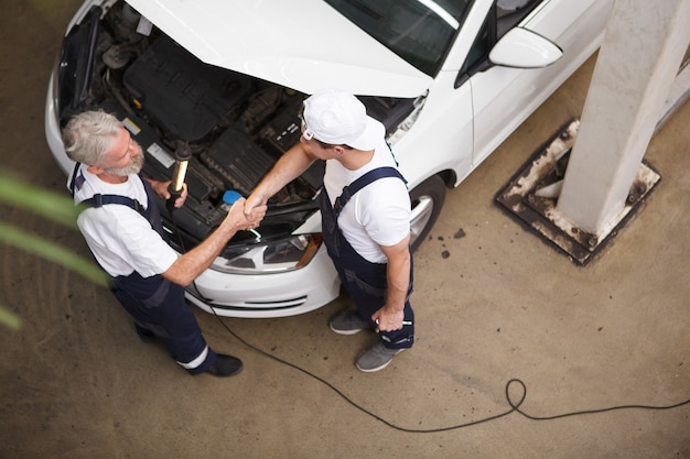 Top view shot of two car mechanics shaking hands over car hood