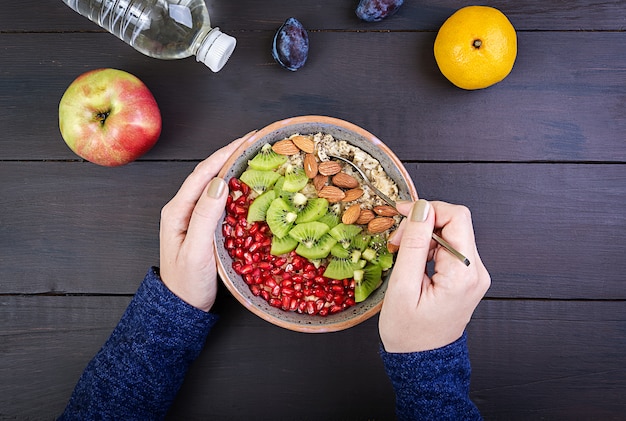 Top view showing hands eating healthy oatmeal with kiwi and almond on a wooden table. 