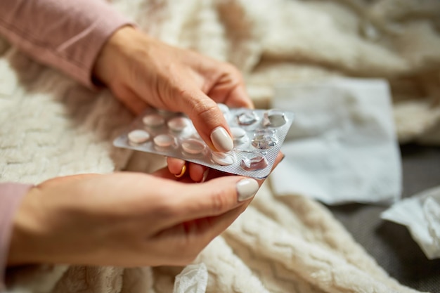 Photo top view sick woman putting medicine in hand and take it, while recovering at home, ill woman taking pill while sitting on couch at home