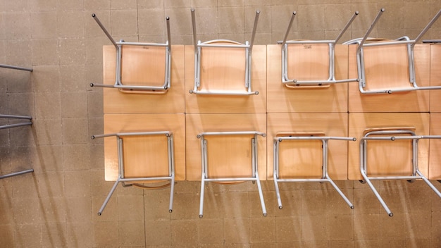 Top view of similar upside down chairs placed on wooden table in light classroom in school.